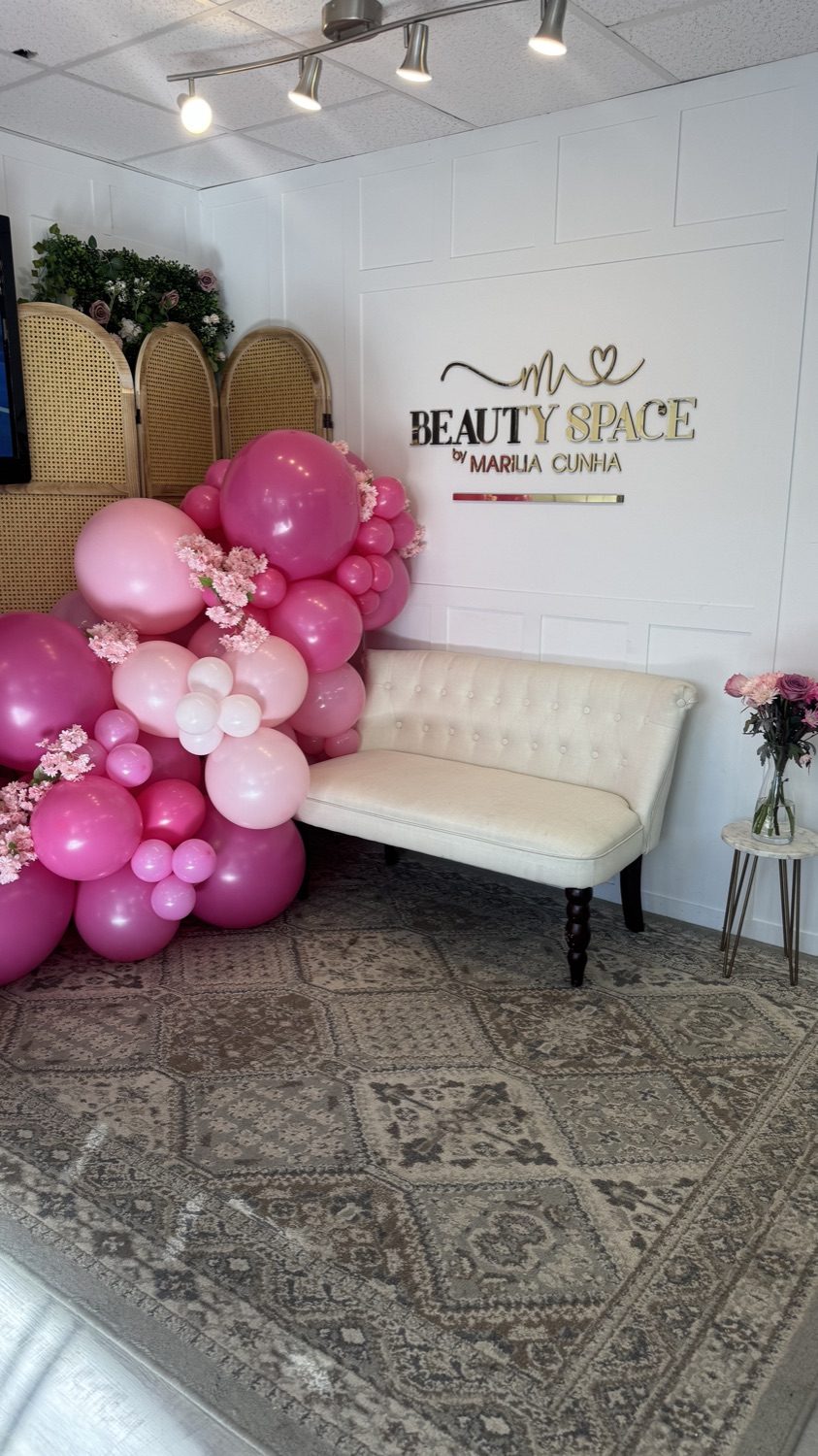 Beauty Space reception in Dracut, MA — the brand logo on the wall, pink balloon arch and a cream sofa